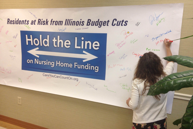 A caretaker at Heritage Health in Bloomington signs the "Hold the Line" banner that will be sent to lawmakers in Springfield to protest potential Medicaid cuts. (Joe Ragusa/WJBC)